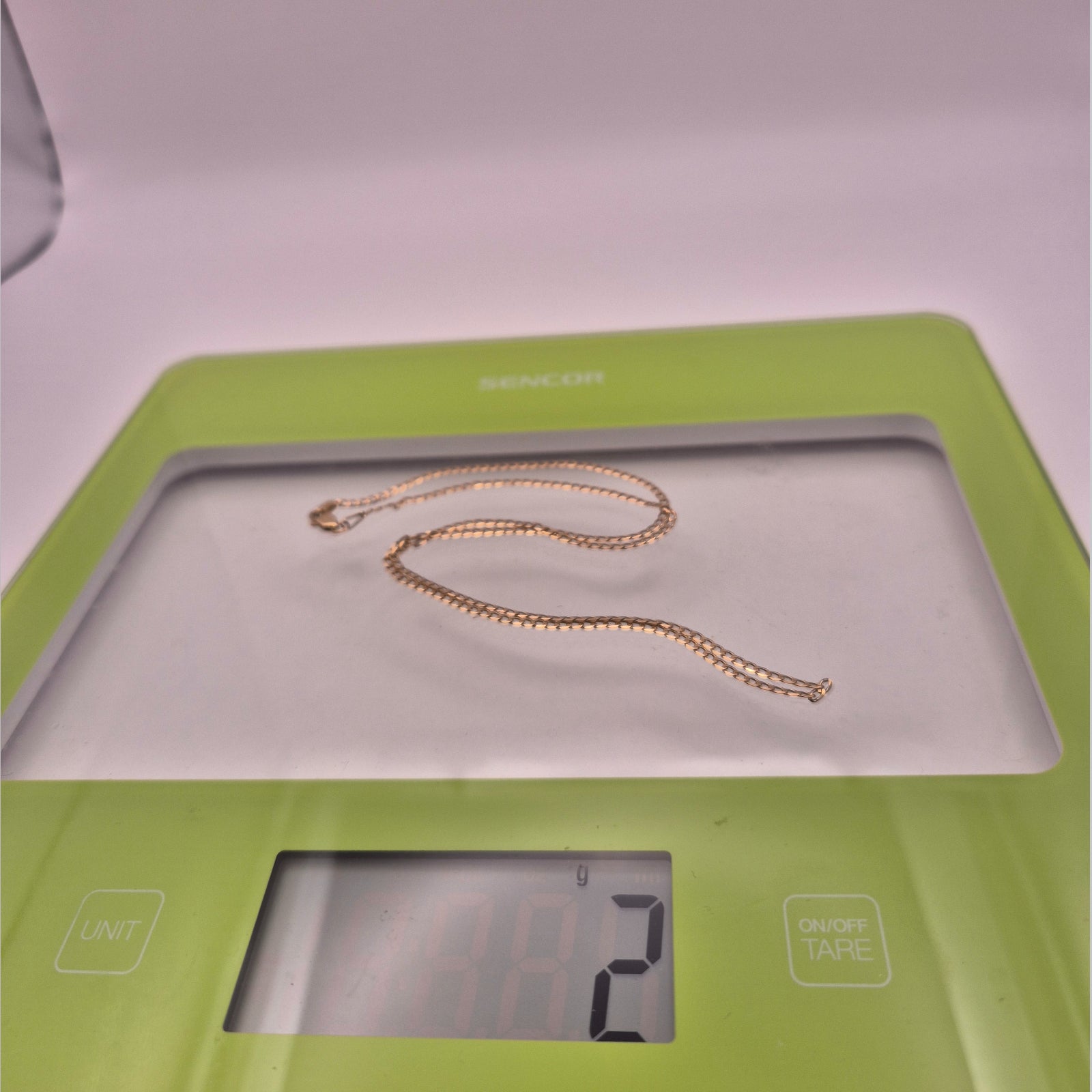 Gold necklace on a digital scale with a green base