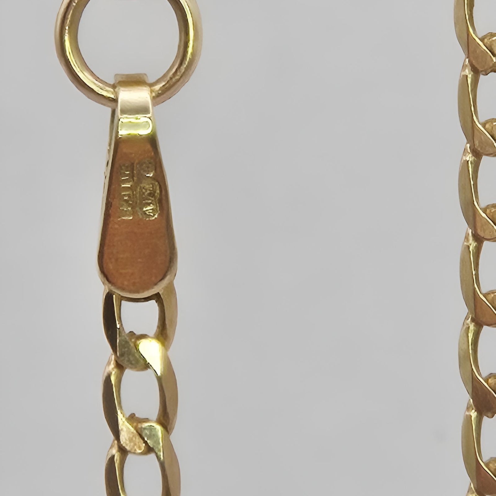 Close-up of a gold chain with a visible brand logo on a gray background